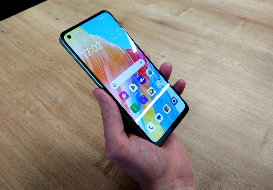smartfon oppo a 78 w kolorze turkusowym jest trzymany w ręce nad drewnianym stolikiem