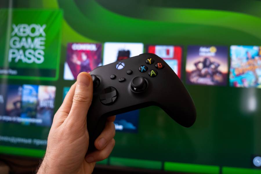 Kontroler do Xboxa trzymany w dłoni na tle ekranu z wyświetlonym menu Xbox Game Pass