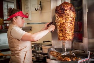przygotowanie mięsa do kebaba- kobieta kroi nożem mięso