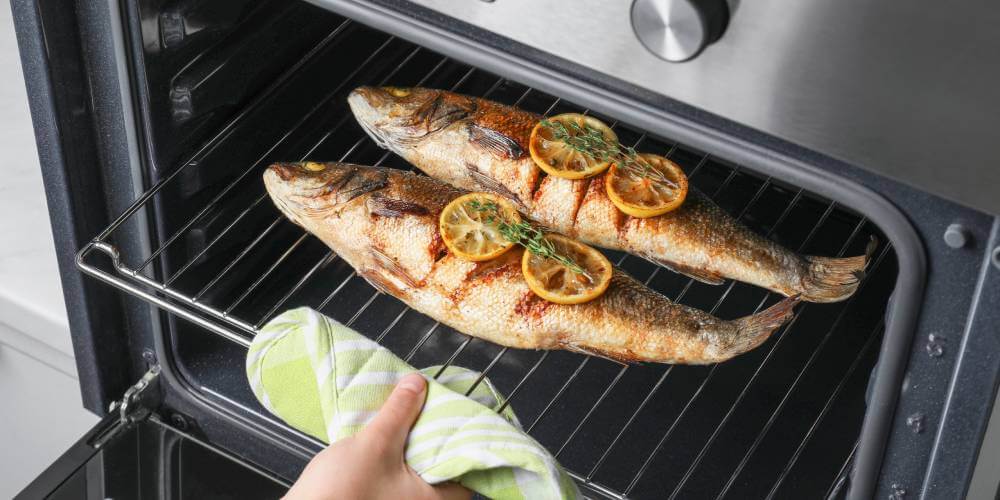 Kobieta wyjmuje z piekarnika rybę, którą przygotowała z użyciem funkcji grill w piekarniku