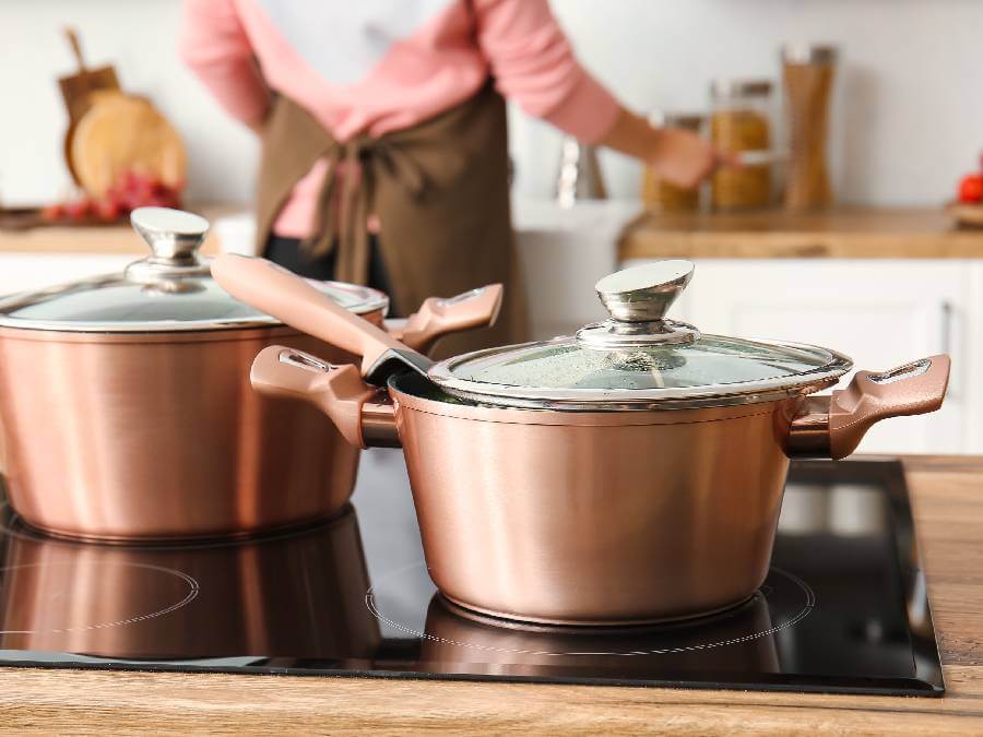 Dwa garnki miedziane ze szklanymi pokrywkami stoją na płycie kuchennej