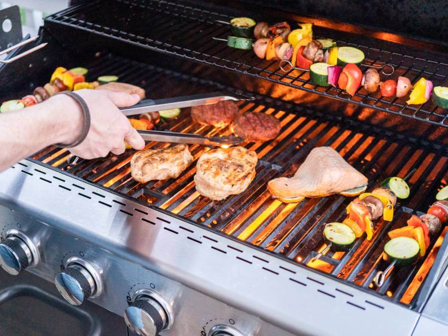 Różnego rodzaju jedzenie przygotowywane na dużym grillu gazowym, zarówno mięso, jak i warzywa