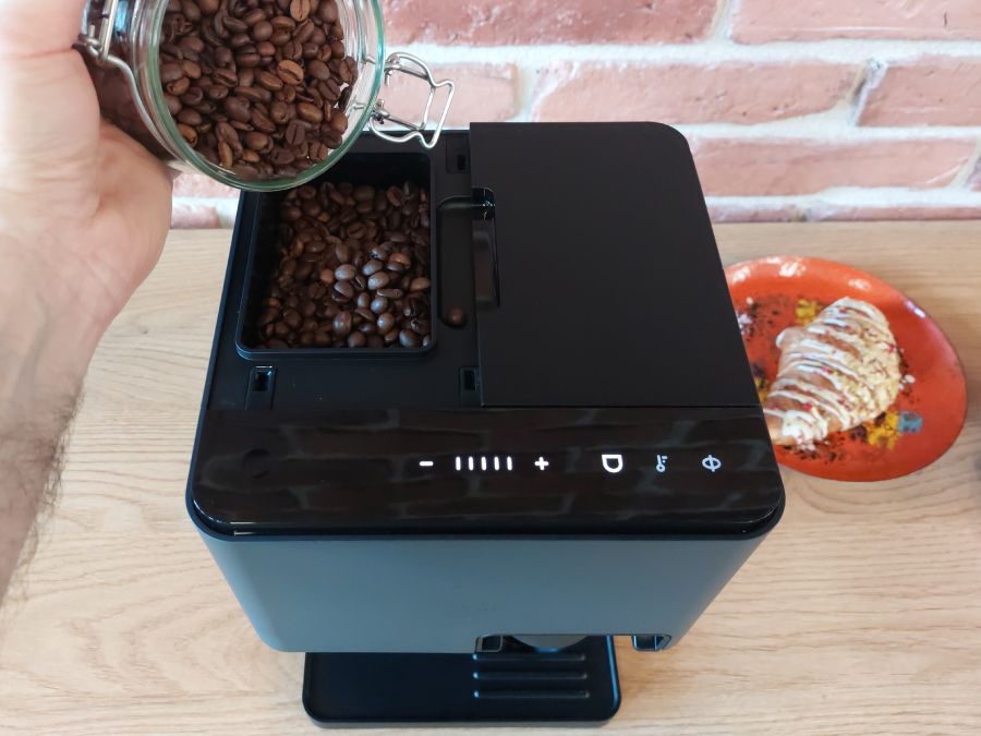 Ktoś wsypuje ziarna kawy do młynka w ekspresie Nivona Cube