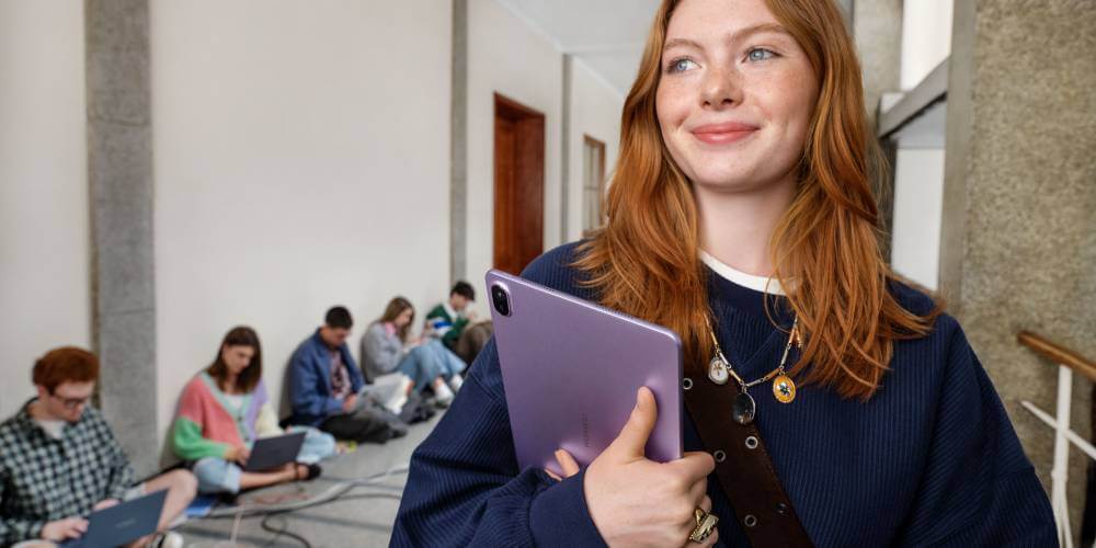 Młoda dziewczyna, studentka, idzie korytarzem na uczelni i trzyma sw&oacute;j tablet Huawei