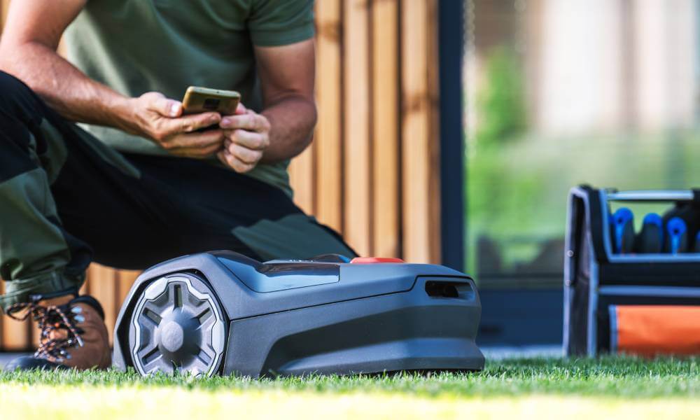 Mężczyzna ustawia parametry pracy robota do koszenia trawy w aplikacji na smartfonie