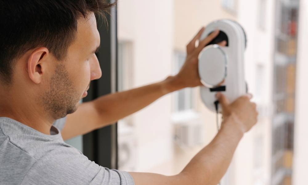 Mężczyzna zdejmuje robota do mycia okien o owalnym kształcie po zakończonej pracy