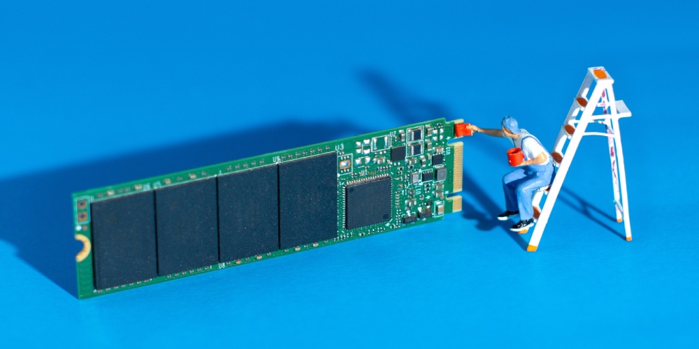 miniaturowy ludzik malujący dysk SSD na niebieskim tle