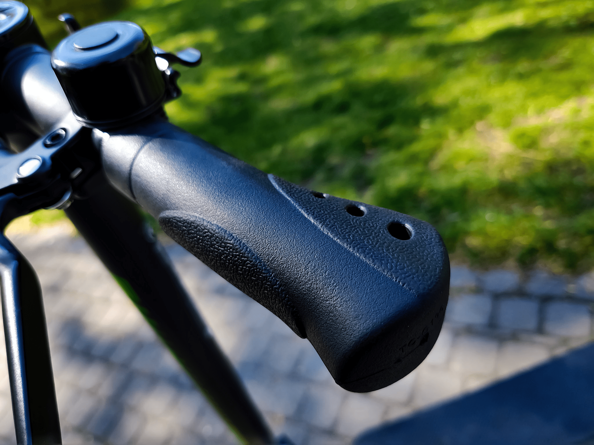 wygodne, bo wyprofilowane rączki hulajnogi acer es series 3. w tle widać dzwonek na kierownicy a także kawałek parku