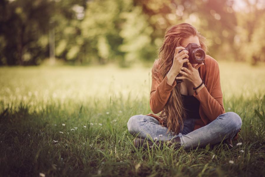 kobieta z aparatem fotograficznym siedzi na trawie