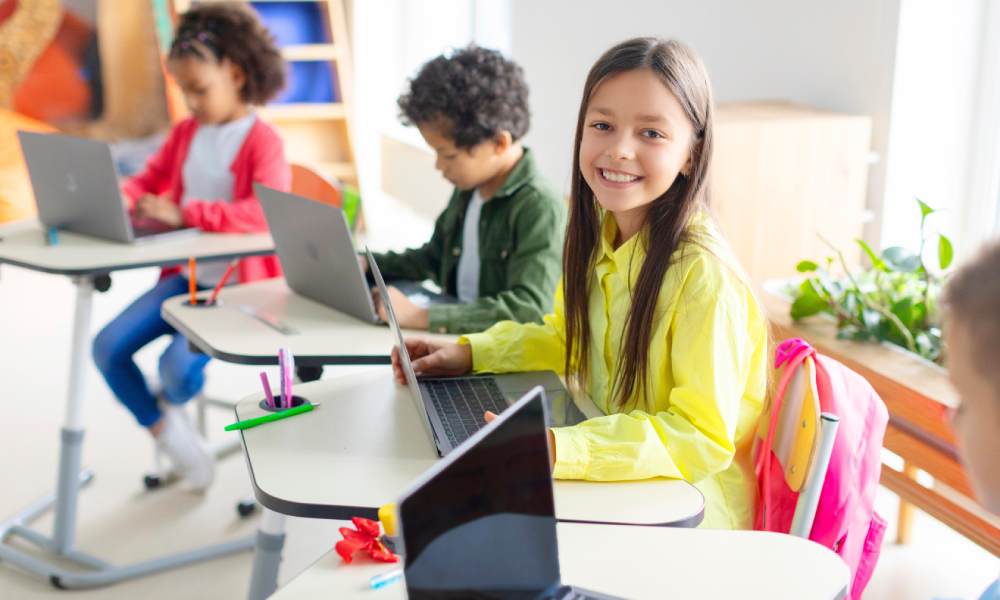 Dzieci siedzące w klasie na lekcji i pracujące z laptopami.