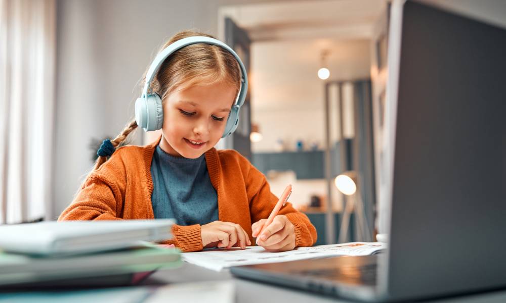 Uczennica w słuchawkach bezprzewodowych siedzi przy biurku przed laptopem.