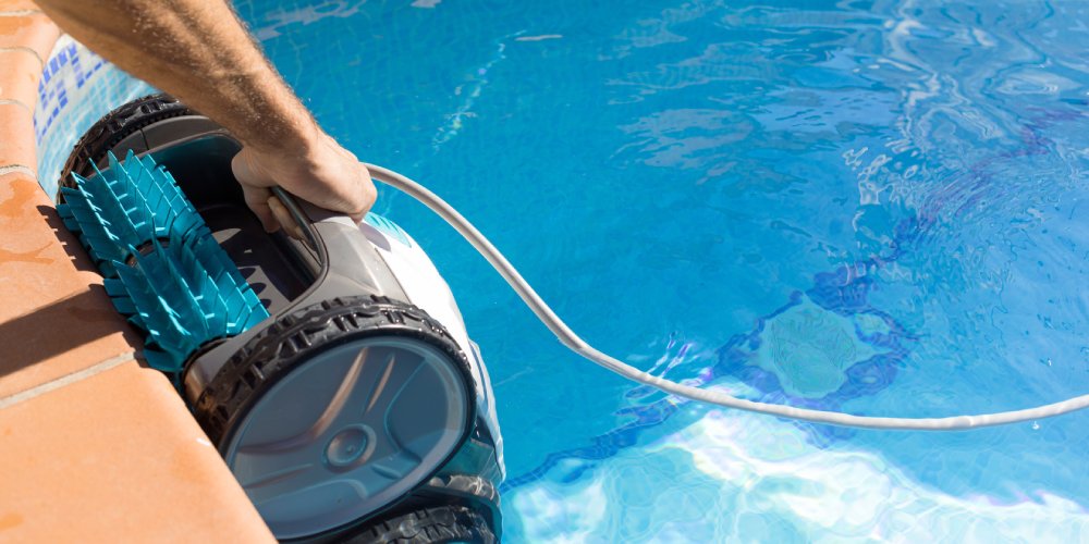 mężczyzna zanurza automatyczny odkurzacz do basenu w wodzie