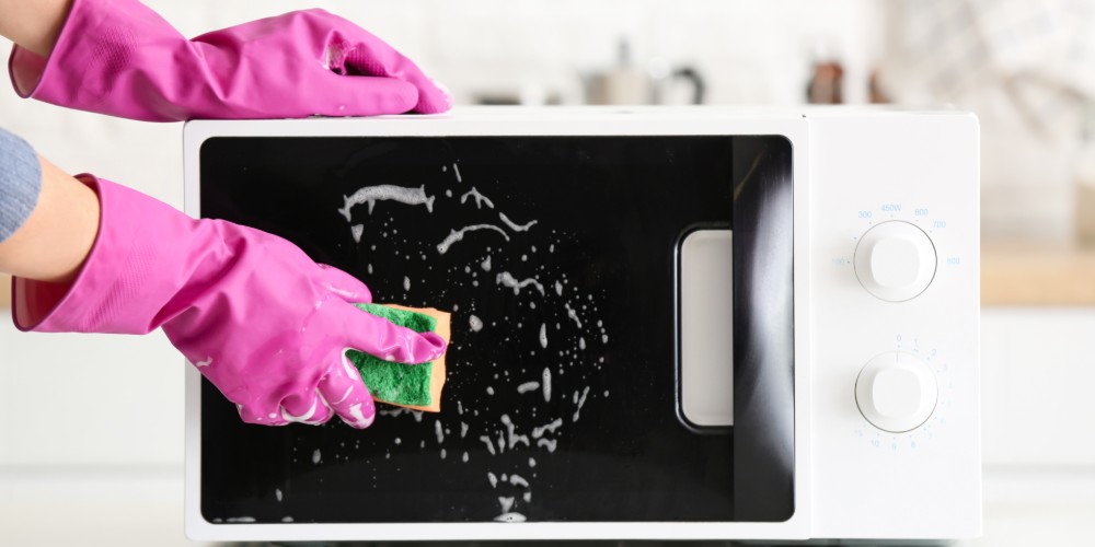 Ręka w rękawicy myjąca drzwiczki mikrofalówki