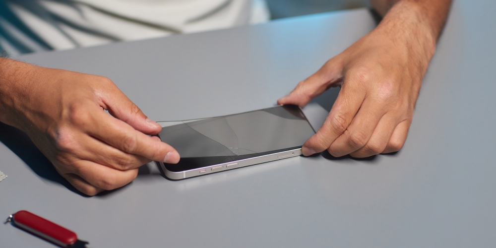 męskie dłonie zdejmujące pęknięte szkło hartowane z telefonu iPhone