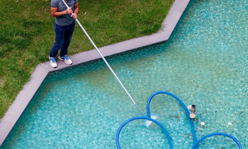 mężczyzna czyści basen odkurzaczem z rurą