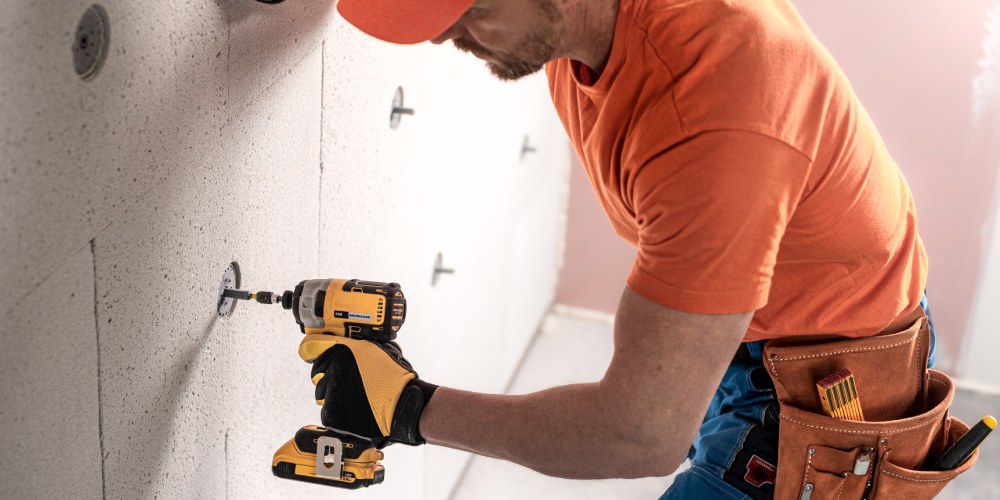 mężczyzna w pomarańczowych ubraniach z kluczem udarowym przy ścianie