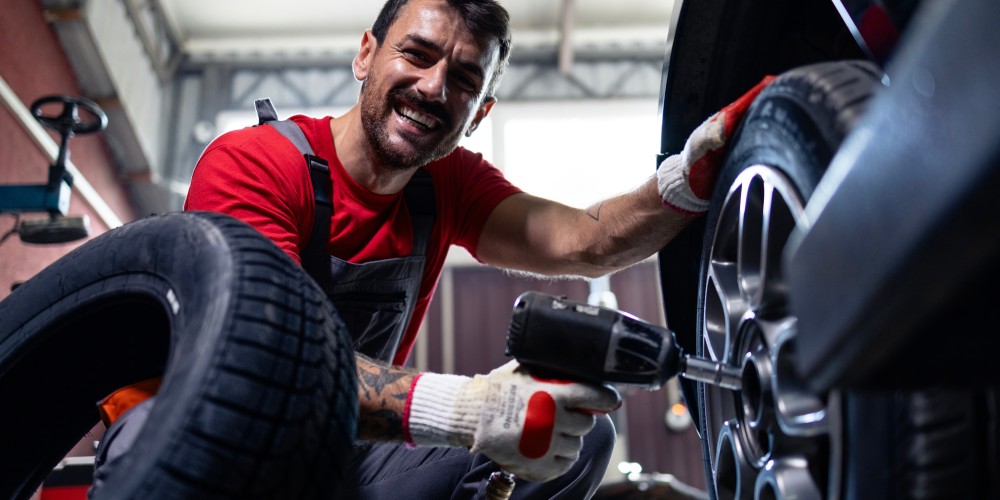 uśmiechnięty mechanik samochodowy trzyma klucz udarowy pneumatyczny