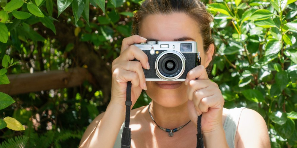 kobieta z aparatem fotograficznym na tle zielonych liści