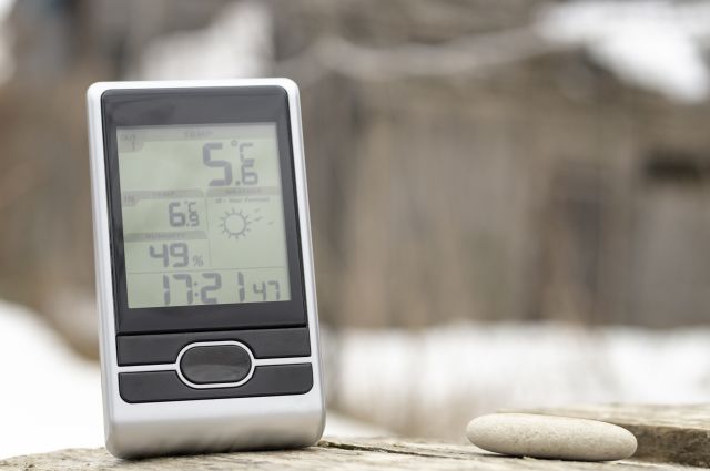 Przykładowy czujnik temperatury zewnętrznej, usytuowany na niewyraźnym tle zimowej zieleni