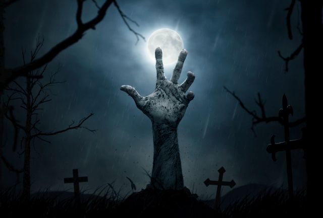 Ręka zombie wychodząca z podziemi na cmentarzu w nocy, konwencja halloweenowa