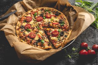 Pizza na papierze i ciemnym stole obok pomidorków cherry