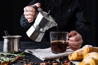 Przelewanie kawy przez baristę z kawiarki do dużej filiżanki na tle croissantów