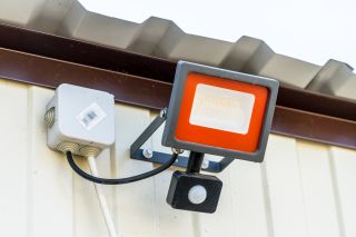 Lampa LED połączona kablami do czujnika ruchu. Oba urzadzenia przymocowaane do ściany.