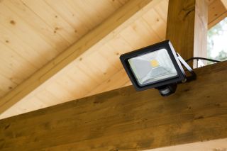 Lampa z czujnikiem ruchu zamontowana na drewnianej belce w altance.