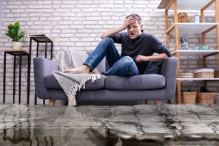 Zdenerwowany mężczyzna siedzący na kanapie zalanego mieszkania
