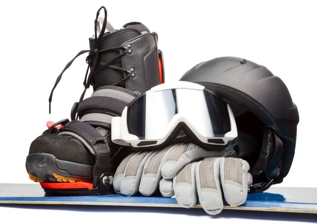 Rękawice narciarskie przykryte goglami pomiędzy kaskiem i butem narciarskim leżą na desce do snowboardingu