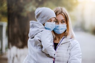 Kobieta w masce antysmogowej trzyma na ręku dziecko, które również ma założoną maskę antysmogową
