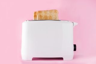 Na różowym tle biały toster załdowany chelebm tostowym