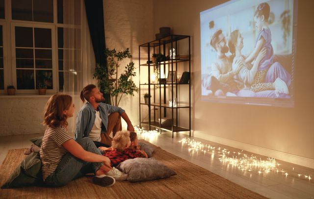 Szczęśliwa rodzina ogląda film wyświetlany przez projektor na ścianę