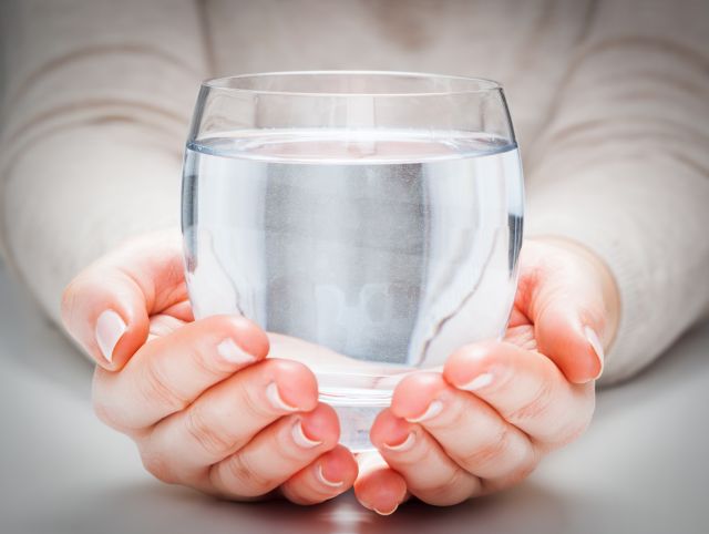 Szklanka z czystą wodą w czyichś dłoniach