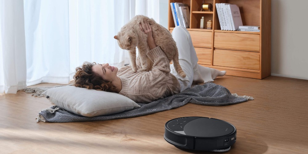 Odkurzacz sprzątający obok kobiety bawiącej się z kotem