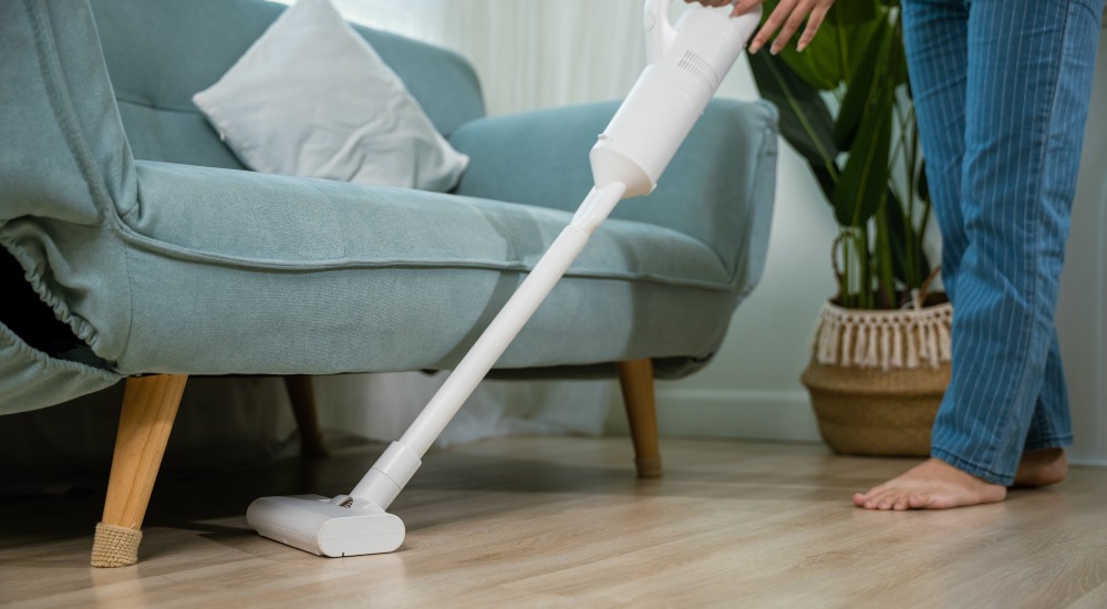 kobieta odkurza pod sofą w salonie