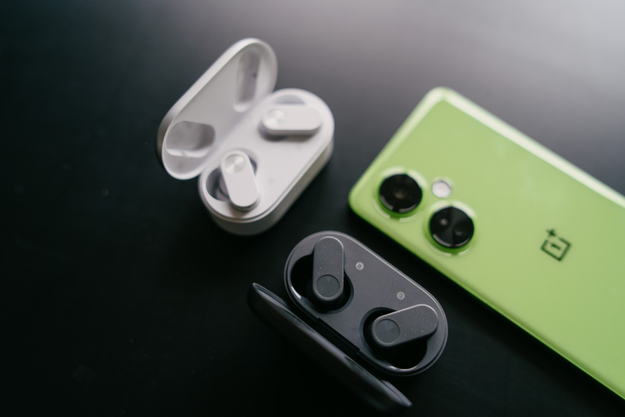 słuchawki OnePlus Nord Buds 2 w dwóch wersjach kolorystycznych w towarzystwie zielonego telefonu OnePlus na czarnym stole