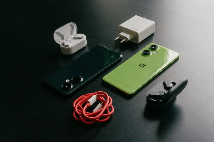 słuchawki OnePlus Nord Buds 2 w dwóch wersjach kolorystycznych w towarzystwie dwóch telefonów OnePlus i akcesoriów na czarnym stole