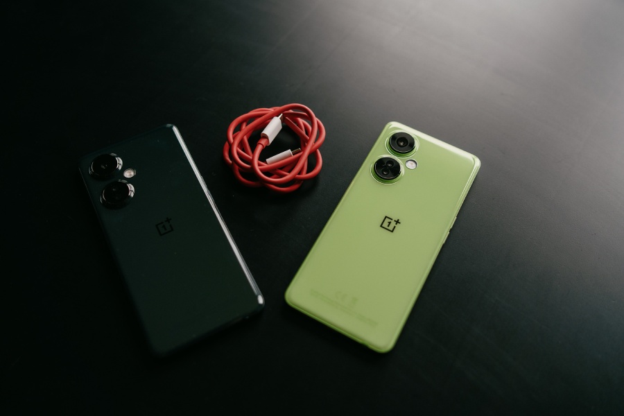 dwa smartfony OnePlus Nord CE3 Lite 5G leżą na czarnym stole wraz z czerwonym przewodem do ładowania
