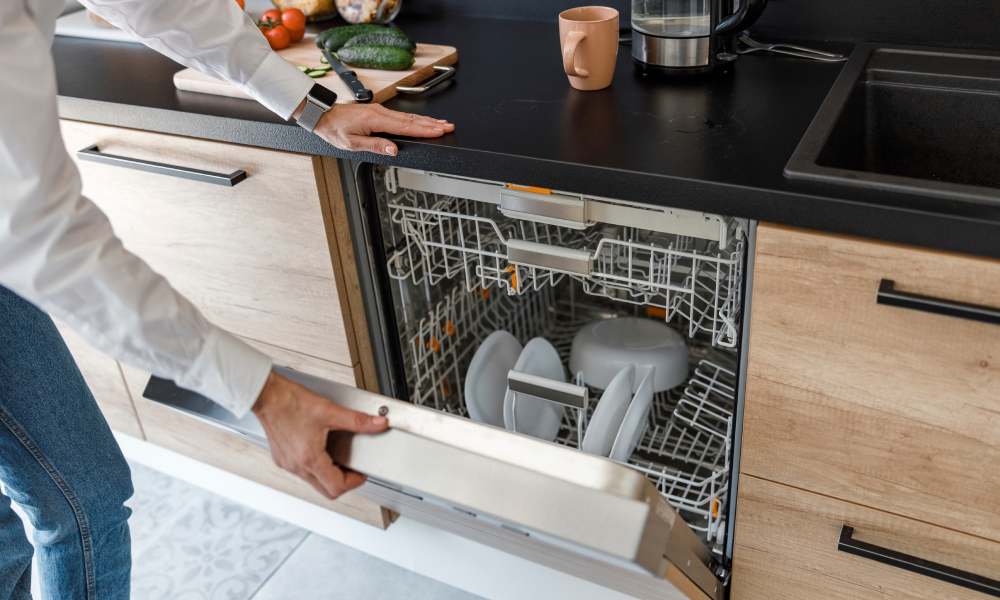 Mężczyzna uchyla drzwi od zmywarki z załadowanymi naczyniami w środku.