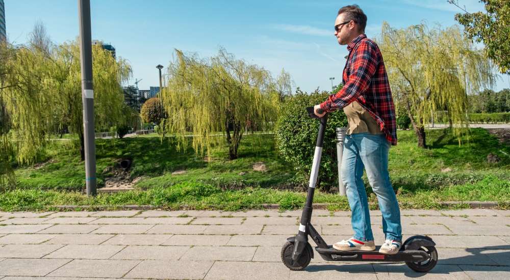 Mężczyzna jadący na hulajnodze elektrycznej po chodniku w parku.