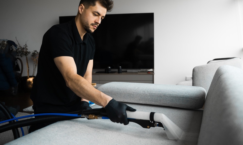 mężczyzna pierze odkurzaczem tapicerkę sofy