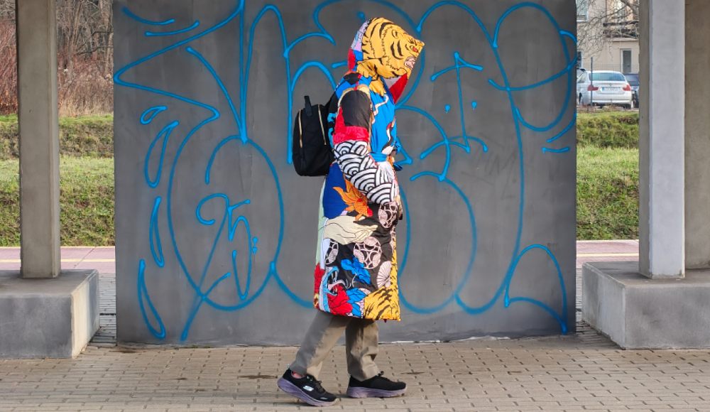 kobieta w kolorowej kurtce na tle szarego murku