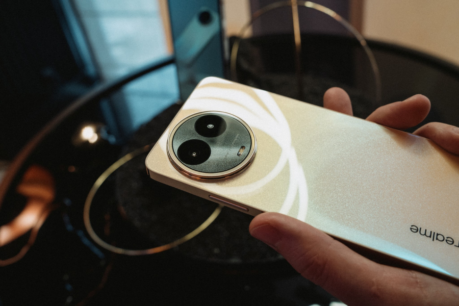 smartfon realme 11 5g w ręku na tle czarnego stolika z wodą i piaskiem