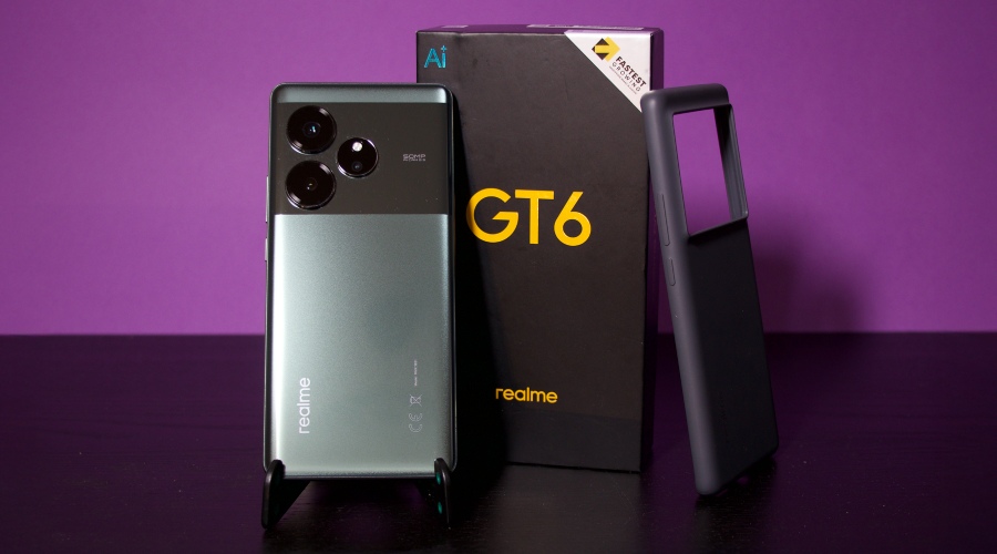 smartfon realme GT 6 stojący obok pudełka i etui na fioletowym tle