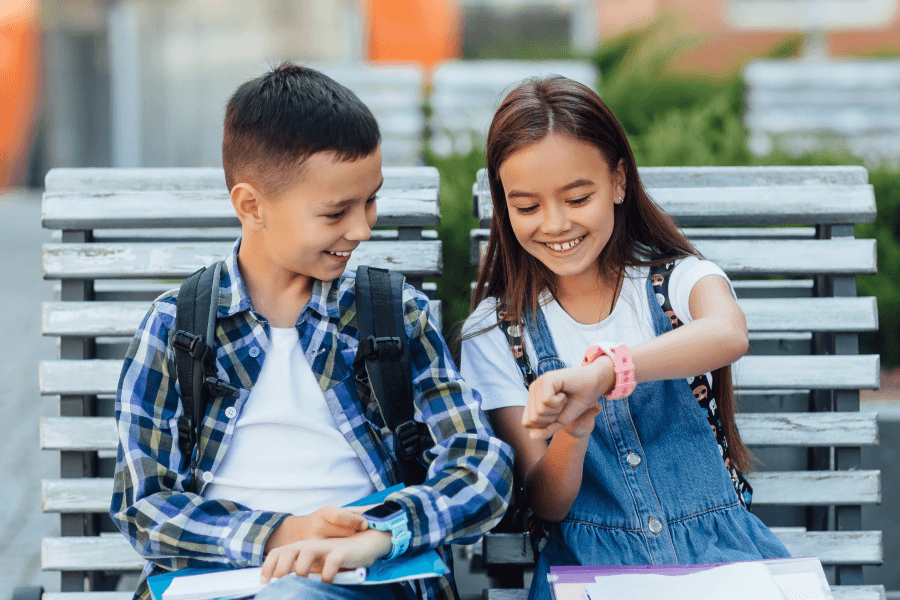 Dzieci siedzą na ławce i pokazują sobie smartwatche