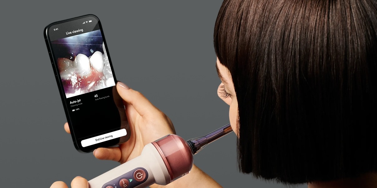 kobieta myje zęby szczoteczką Dyson i ogląda to na telefonie
