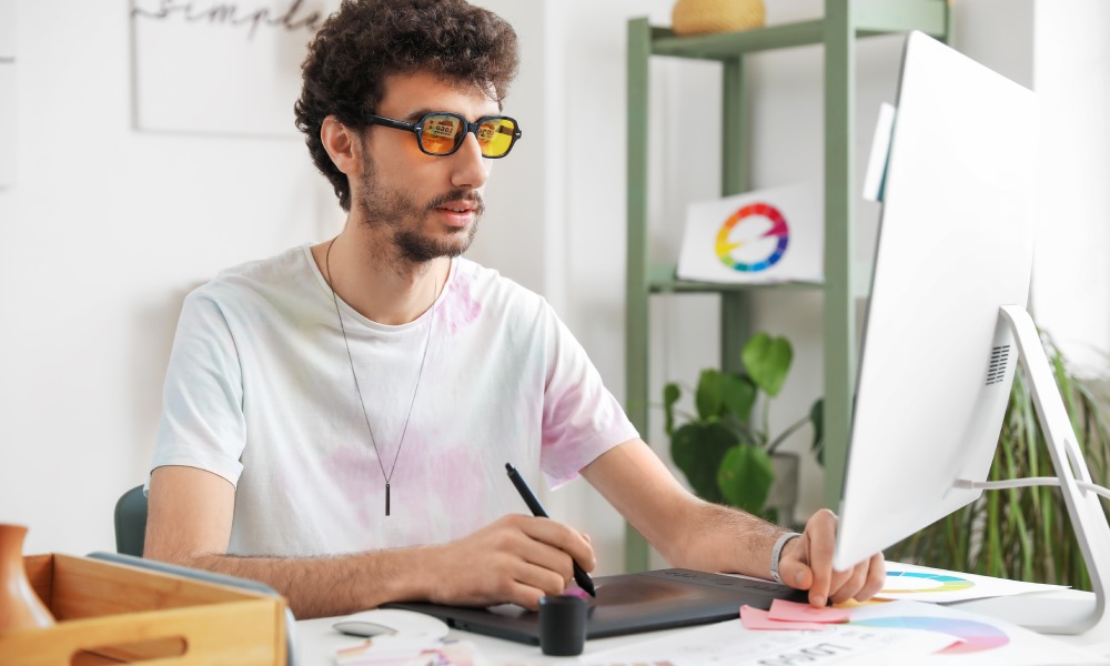 mężczyzna rysuje na tablecie graficznym patrząc w ekran monitora komputera