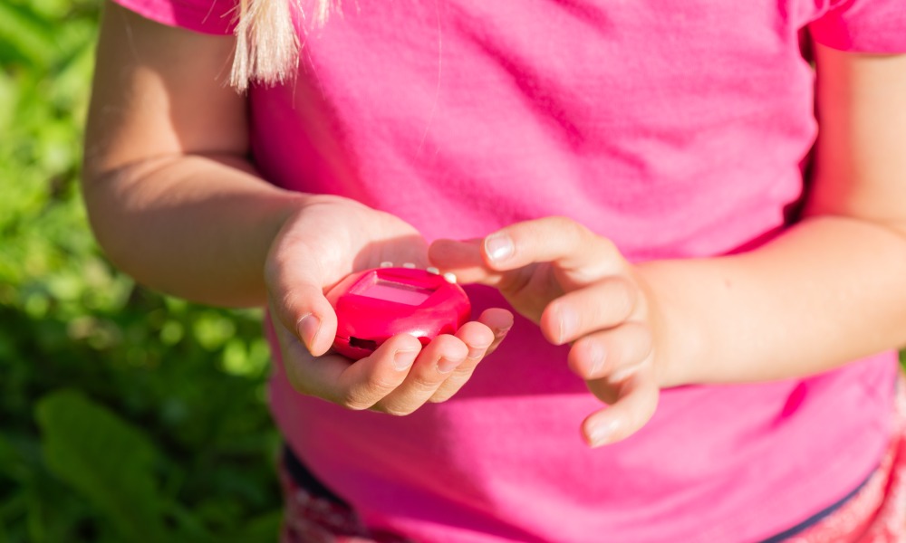 dziewczynka trzyma w rękach zabawkę Tamagotchi