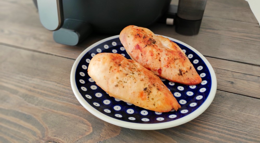 air fryer Philips Ovi NA547 - na talerzu obok air fryera leżą upieczone piersi kurczaka